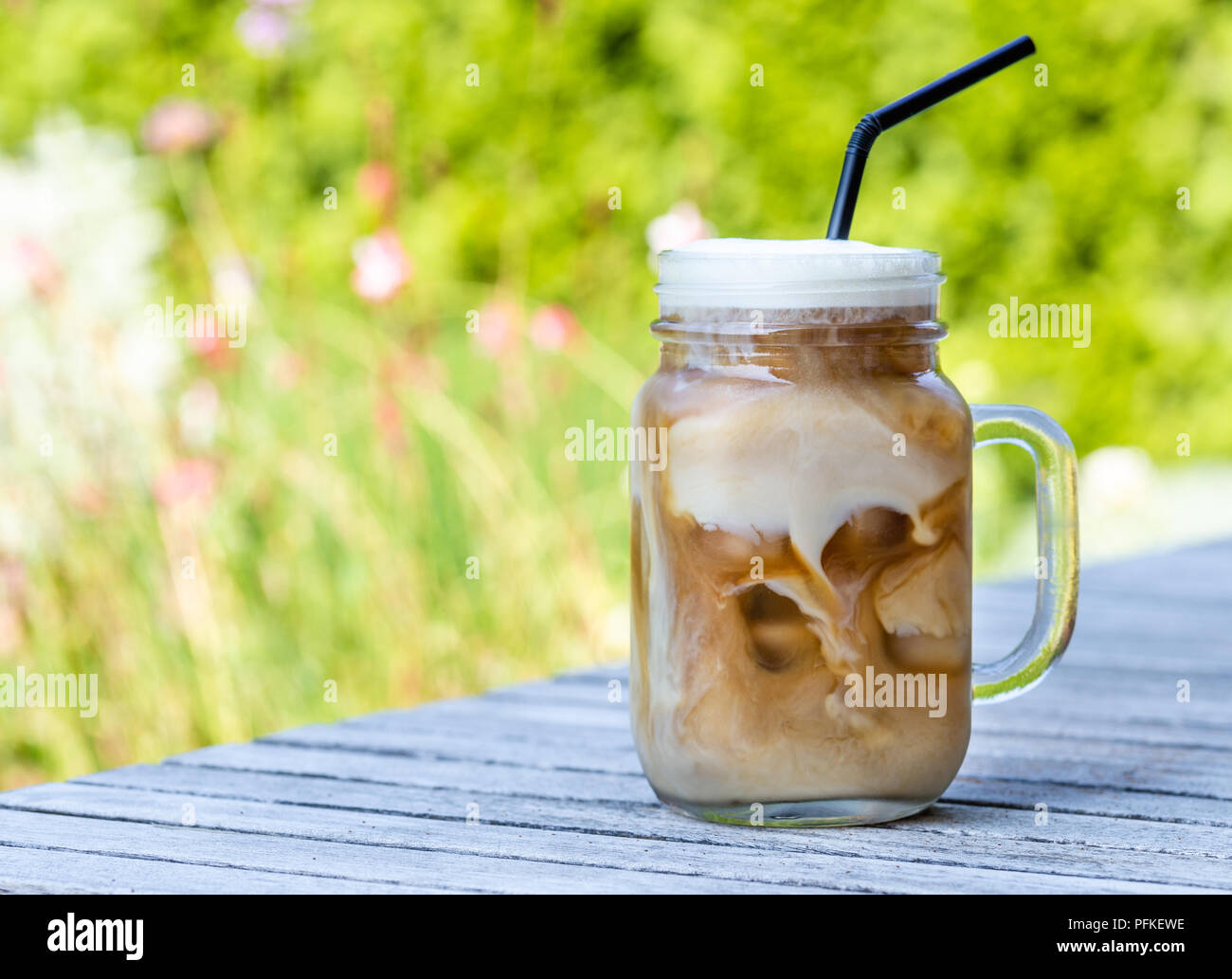 Ice coffee in glass mug with milk and cinnamon on wooden table in