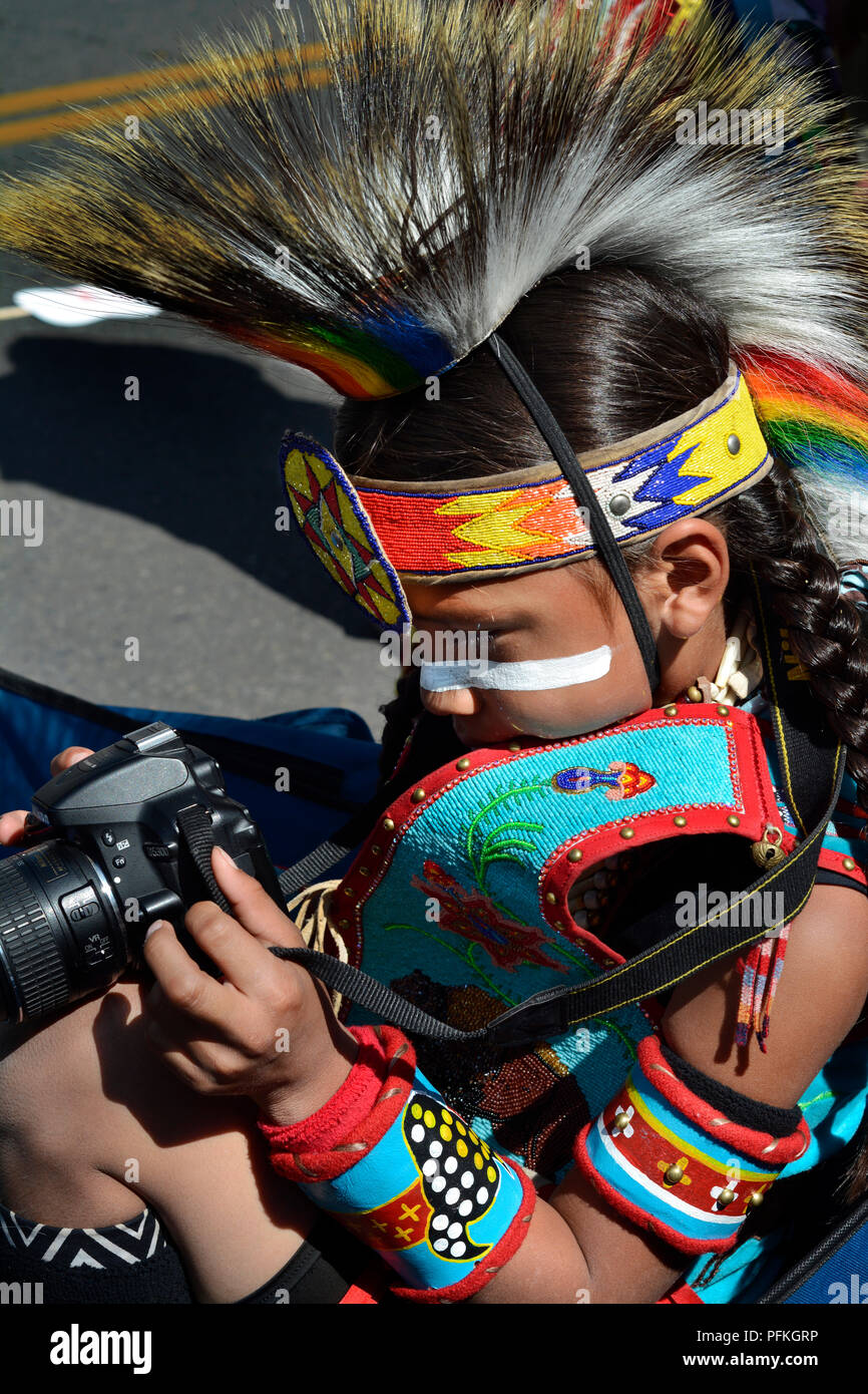 A young Native-American boy wearing traditionall Plains Indian regalia takes a picture with his Nikon camera. Stock Photo