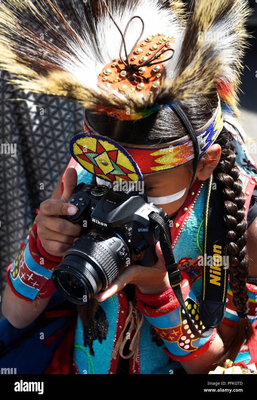 A young Native-American boy wearing traditionall Plains Indian regalia takes a picture with his Nikon camera. Stock Photo