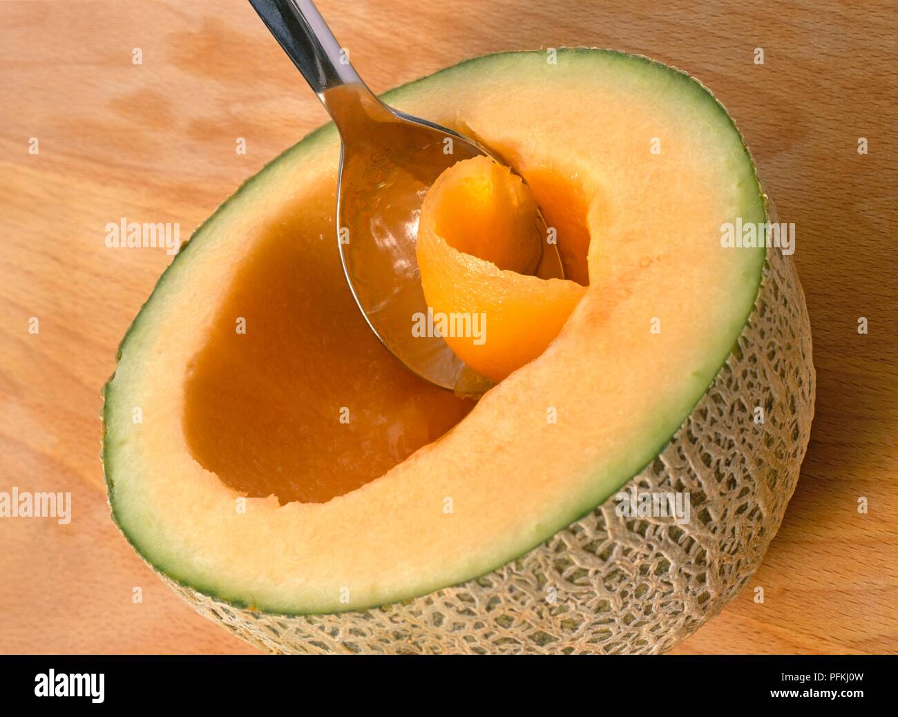 Using spoon to scoop out flesh from cantaloupe melon, close-up Stock Photo