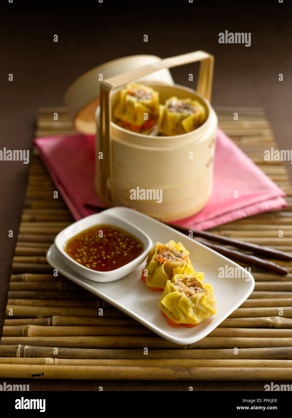 Sui mai, Chinese steamed pork dumplings served on plate with soy and ginger dipping sauce, and in bamboo steamer Stock Photo