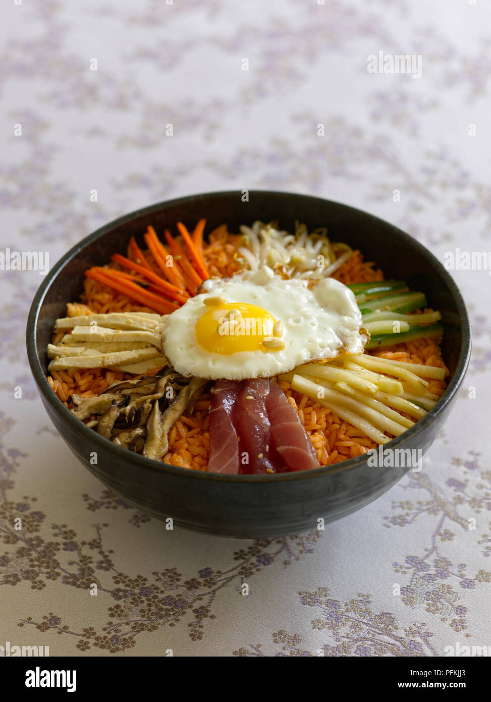 Bibimbap, Korean rice bowl with tuna and vegetables cut into strips, topped with fried egg and pine nuts Stock Photo