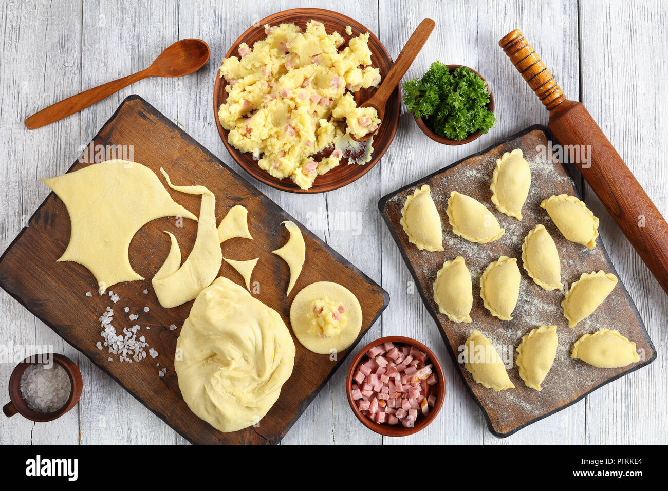 uncooked pierogi - traditional Polish or Ukrainian dumpling is filled with mashed potato, and finely chopped ham or bacon on wooden cutting board with Stock Photo