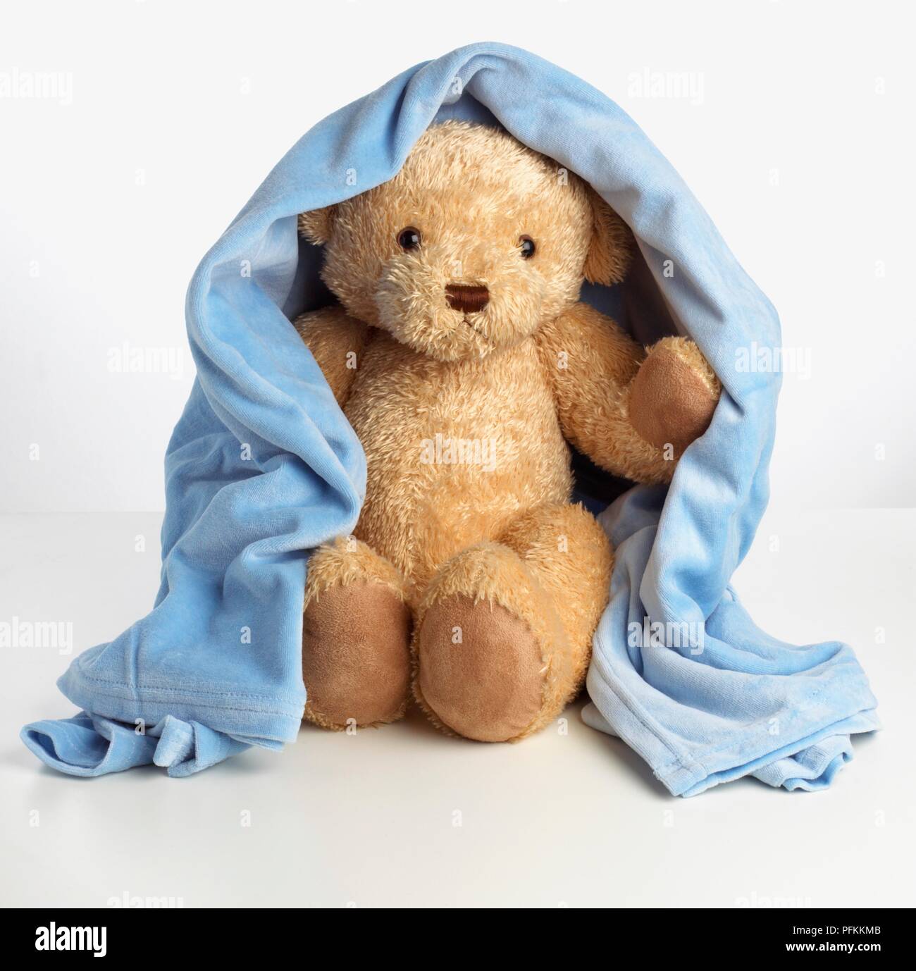 A teddy bear covered with a blue blanket Stock Photo