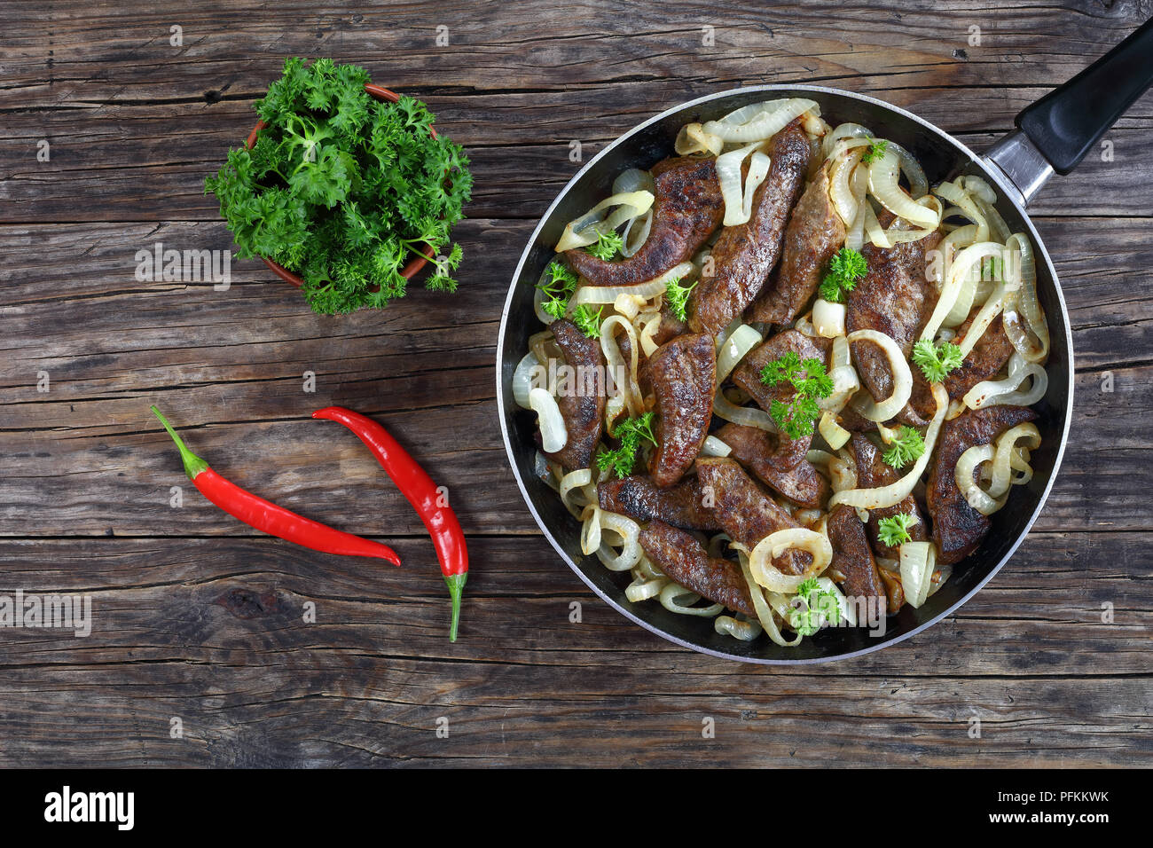 delicious Fried veal liver with onion rings in skillet on dark wooden
