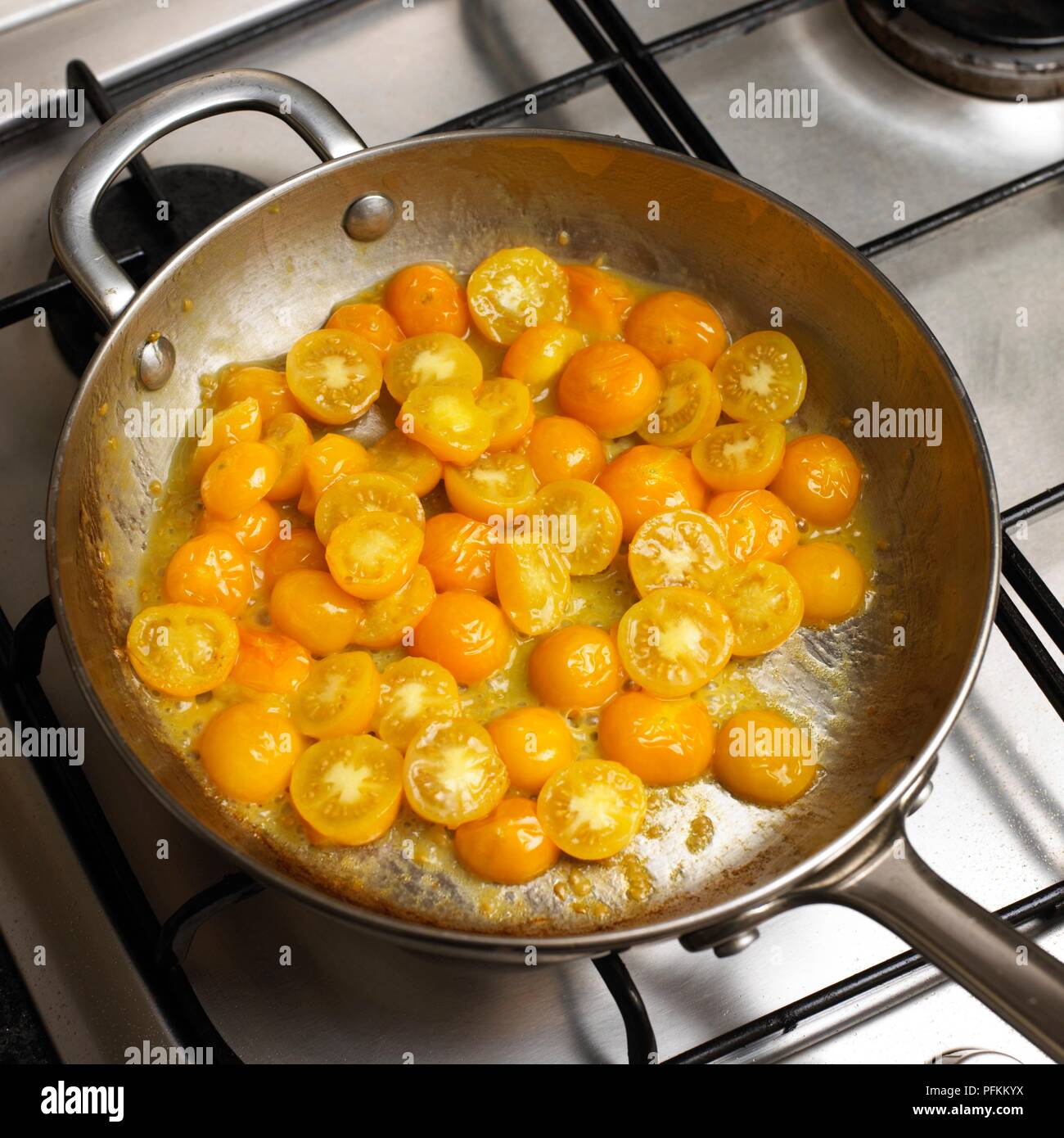 Pan-frying yellow tomatoes on gas hob Stock Photo