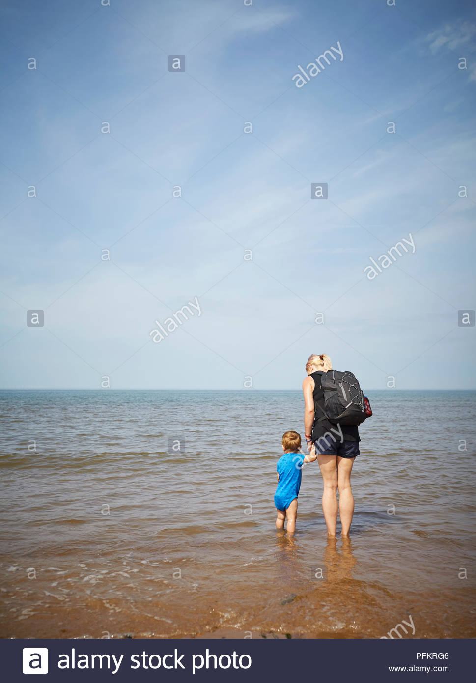 Mum And Baby Son Standing In The Sea Looking Out To The Horizon On