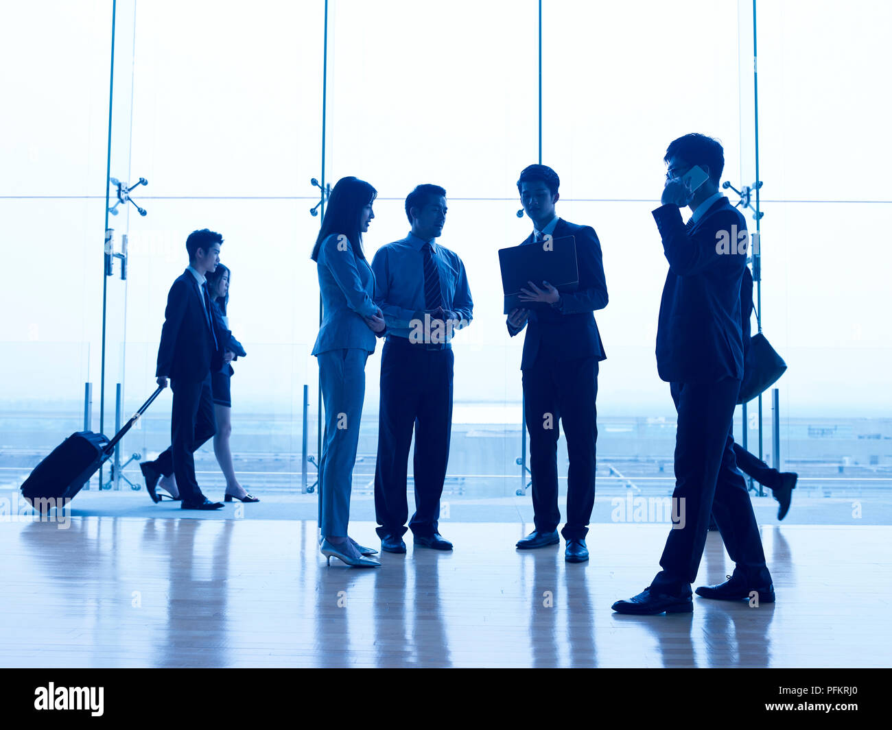 silhouettes of asian corporate executives discussing business in airport terminal building. Stock Photo