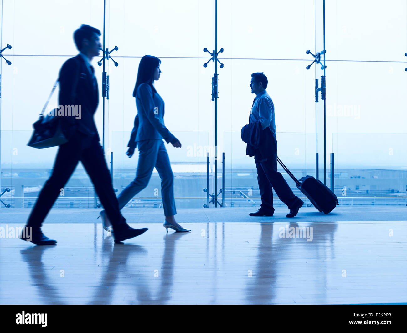 asian business people walking in airport terminal building, focus on the background. Stock Photo