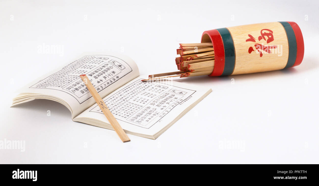 Divination sticks in a pot, next to open book showing Chinese script Stock Photo