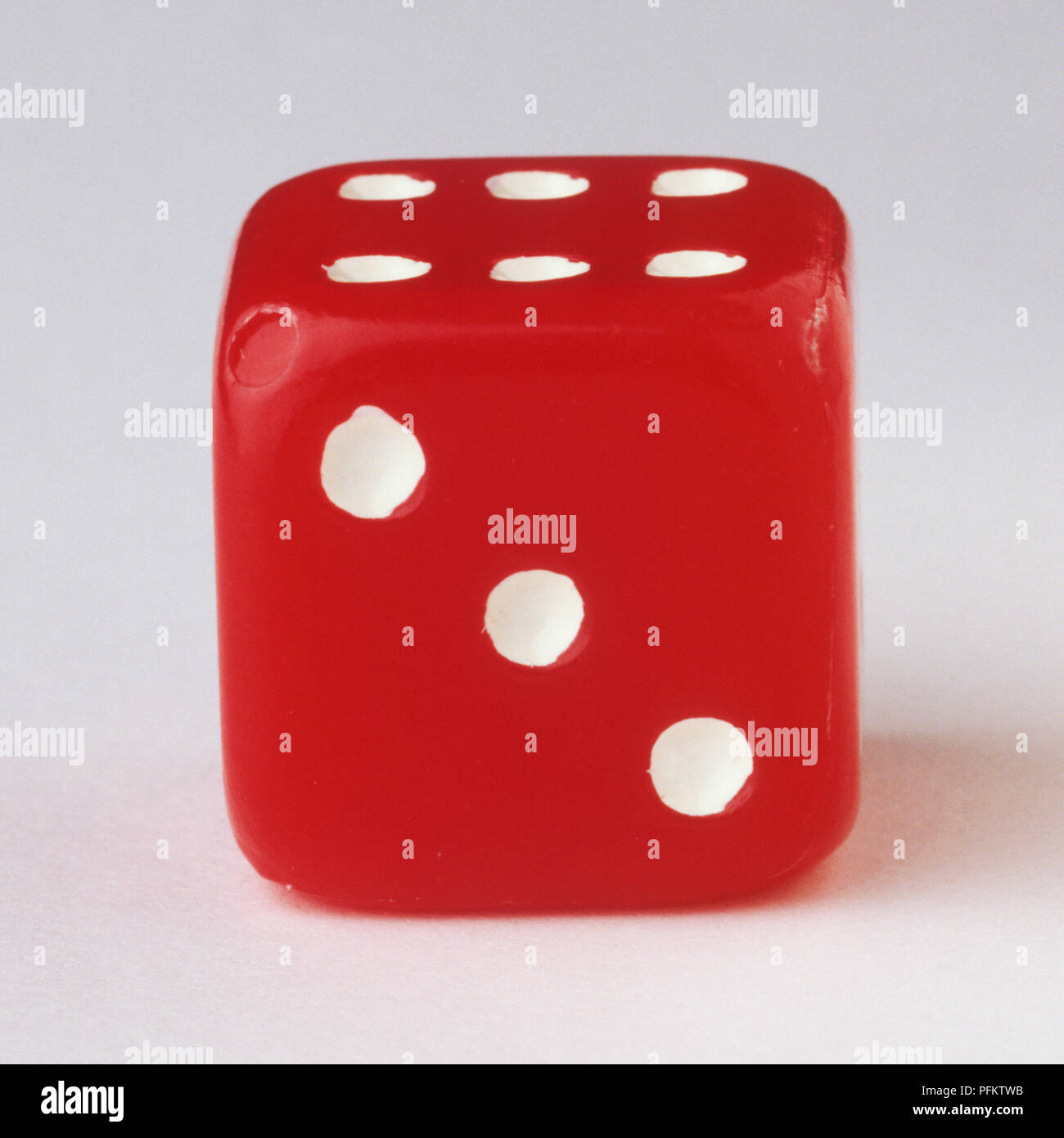 One red dice showing three white dots. Stock Photo