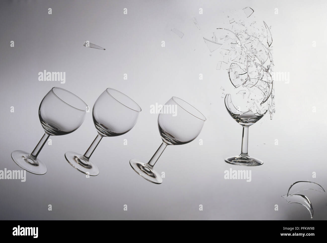 Photographic print depicting four wine glasses, one of them broken with the base surrounded by pieces of glass. Stock Photo