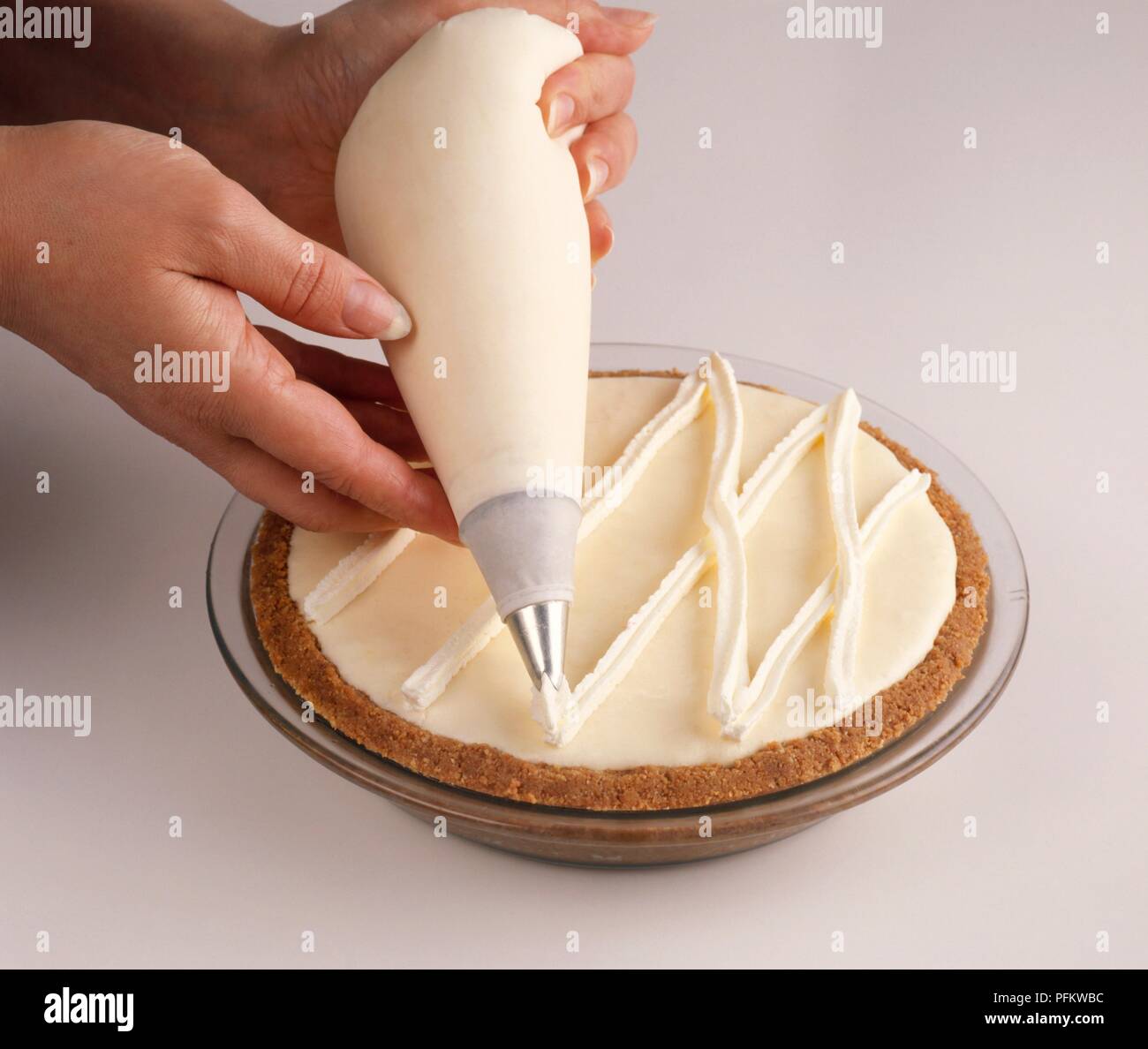 Whipped cream being piped over the top of a pie in a lattice design