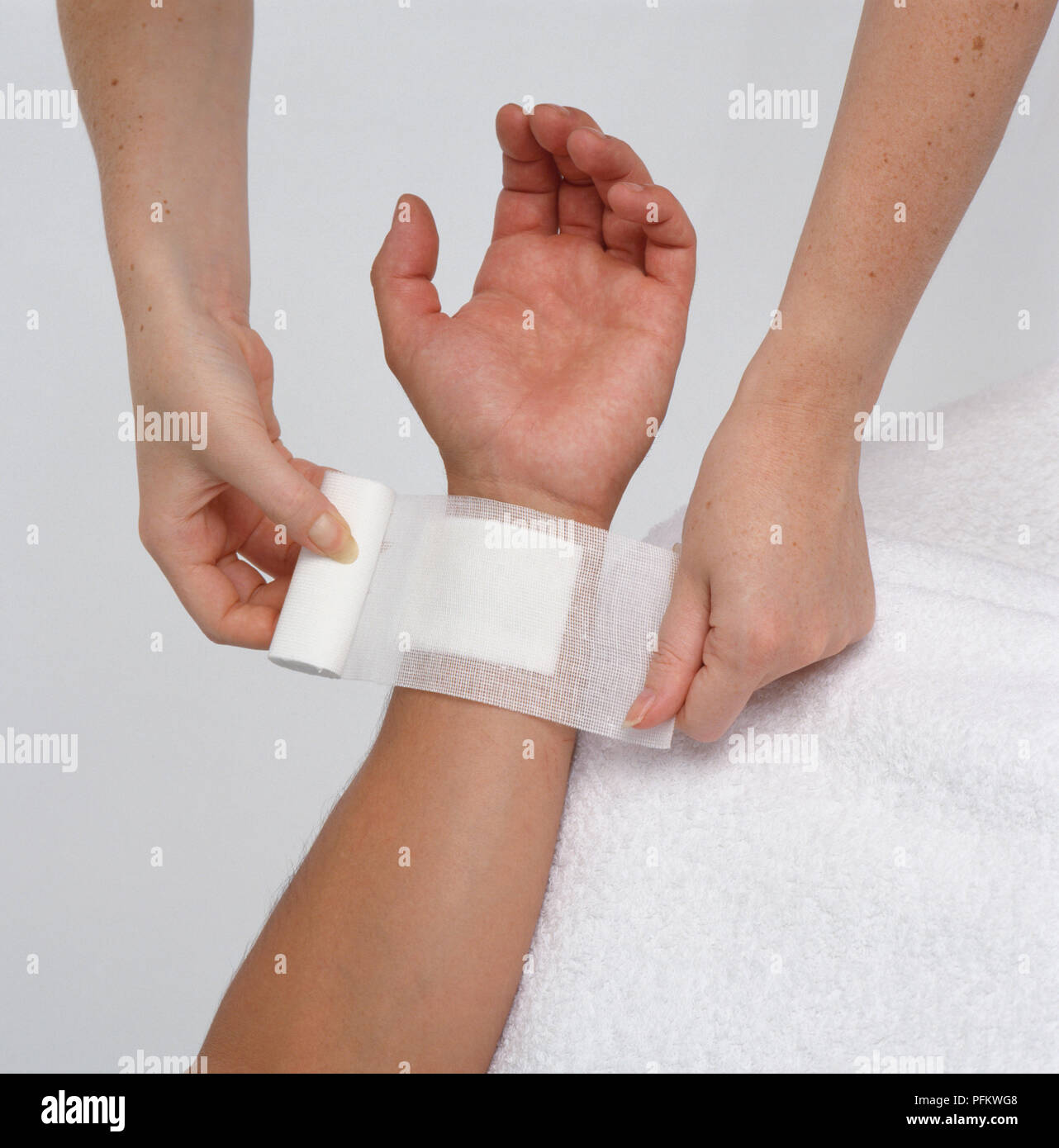 Woman's hands covering wound on boy's wrist with bandage, closeup