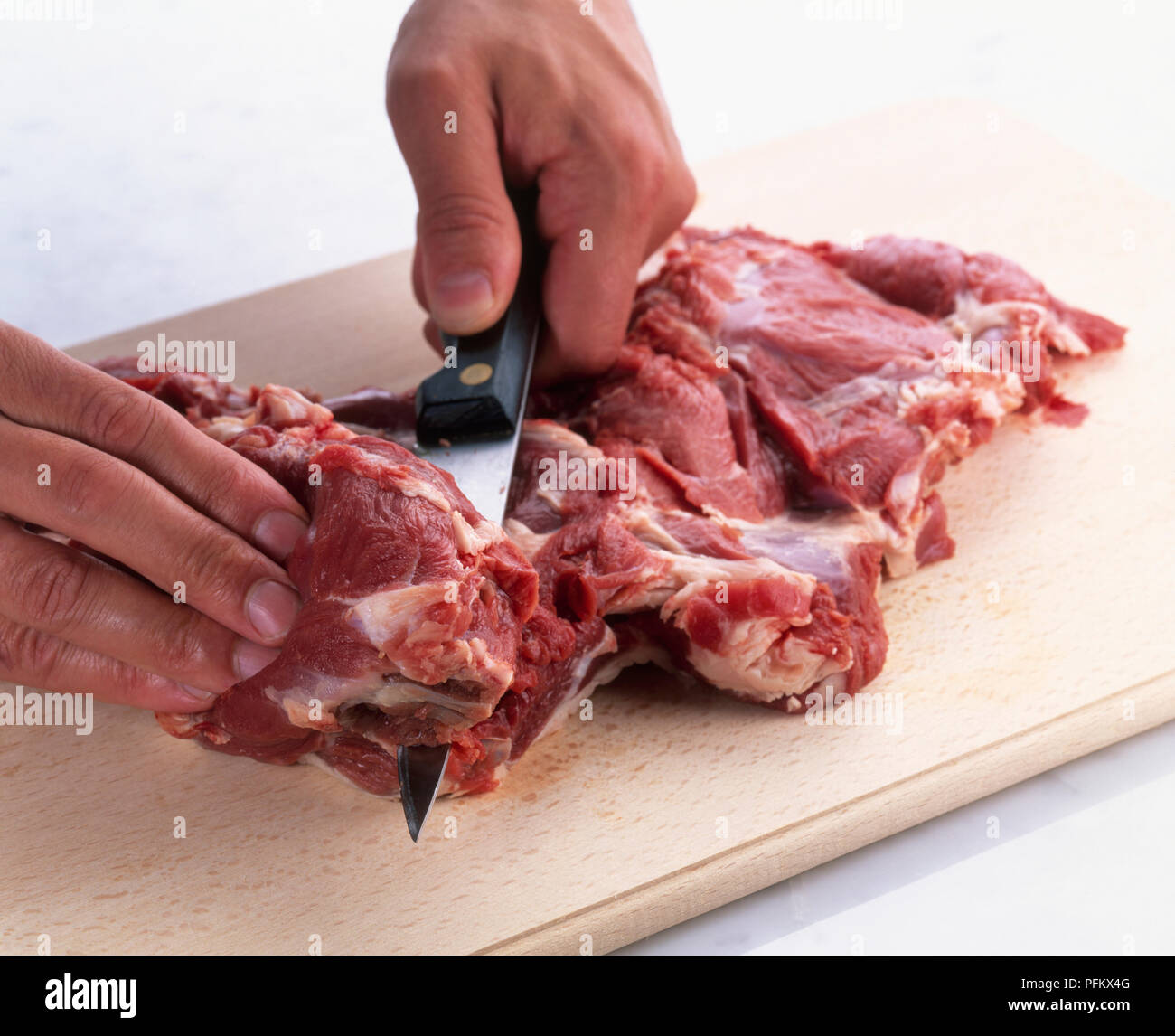 Butterflying leg of lamb using knife to make cut along thick part of meat next to hole left by bone Stock Photo