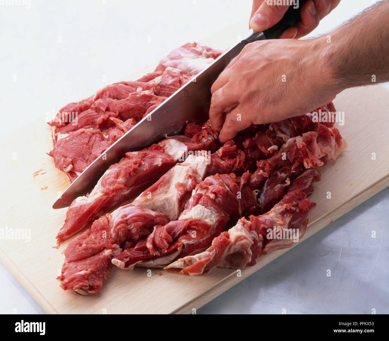 Boning leg of lamb using knife to cut through meat on either side of blade bone Stock Photo