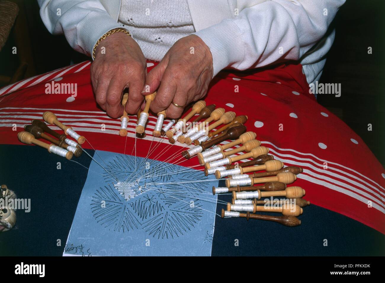 Belgium, Bruges, close-up of woman's hands making lace with bobbins on lap Stock Photo