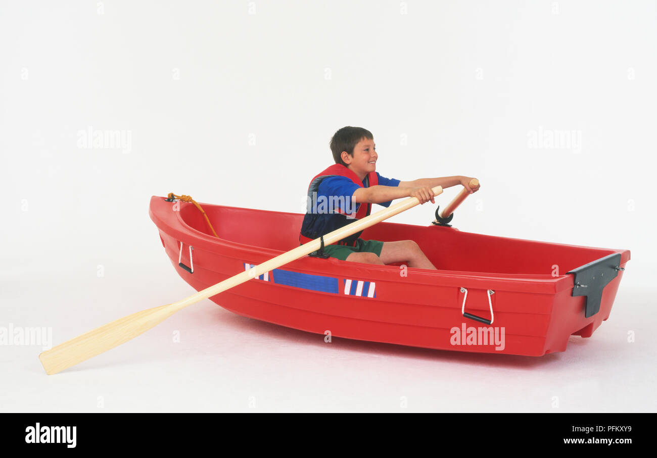 A boy wearing a life jacket sitting in a red rowing boat, holding