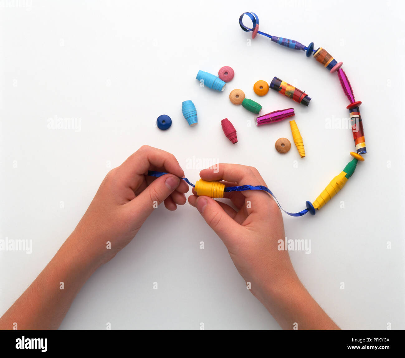 Girl's hands threading colourful paper beads onto ribbon, closeup