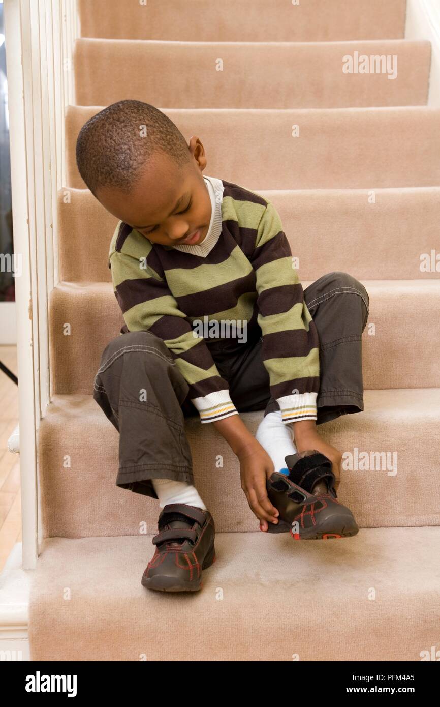 Boy sitting on stairs putting his shoes on Stock Photo - Alamy