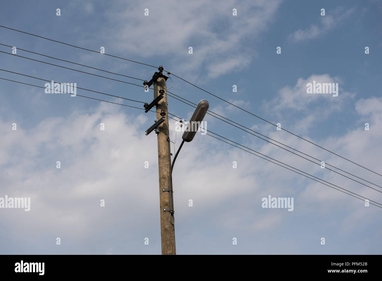 Wooden street lamp post with electric wires against blue sky with white clouds Stock Photo