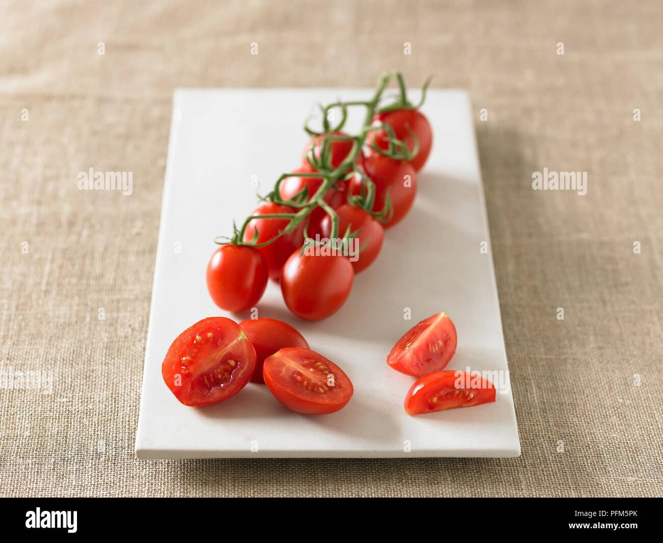 Plum tomatoes on vine and sliced on plate Stock Photo