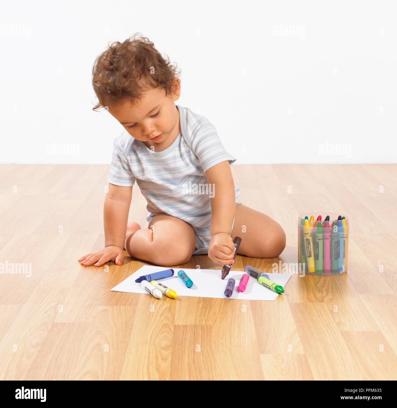 Baby boy sitting on floor drawing with wax crayons Stock Photo