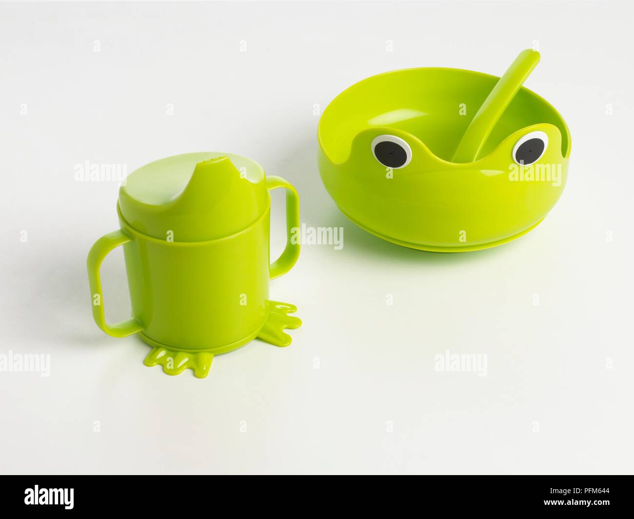 Green plastic bowl with anthropomorphic face on the front, and a plastic cup with spout and tiny feet Stock Photo