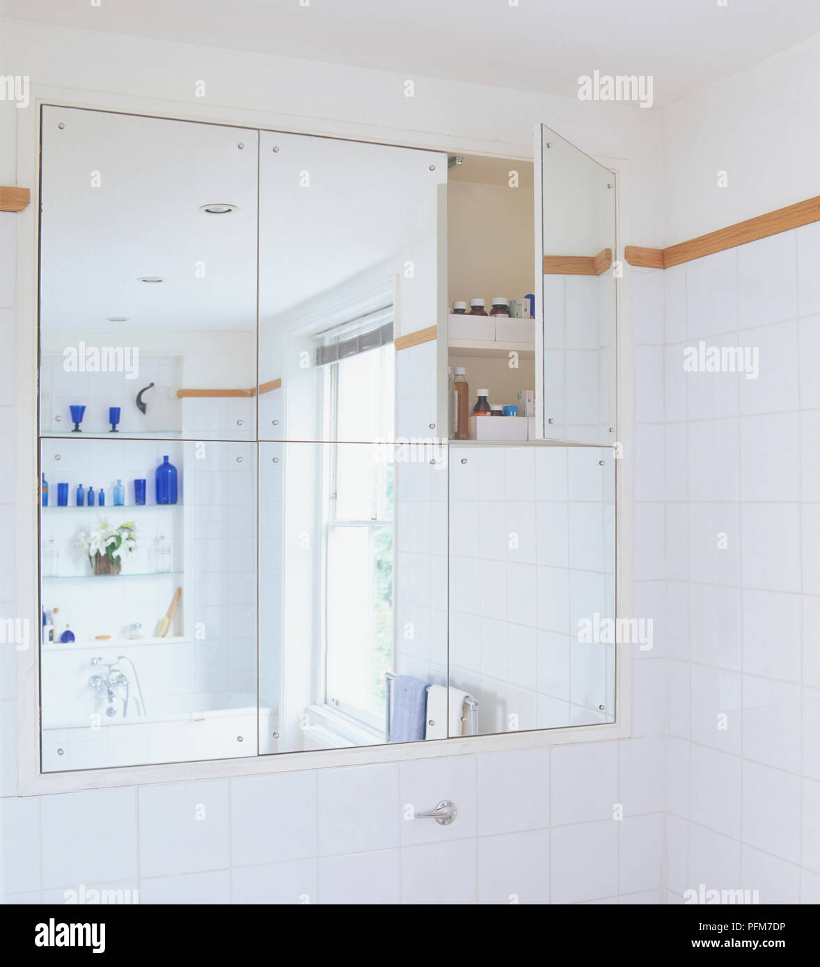 Reflection of white tiled bathroom in mirror which also acts as hidden cupboard Stock Photo