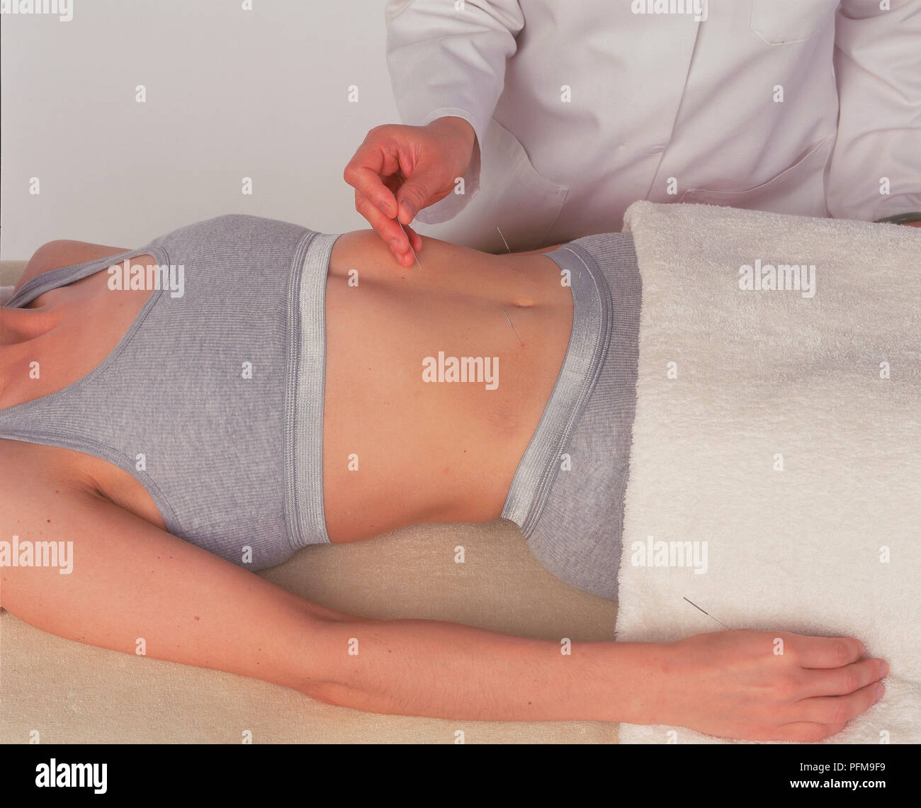 Practitioner inserting acupuncture needle into patien'ts abdomen, side