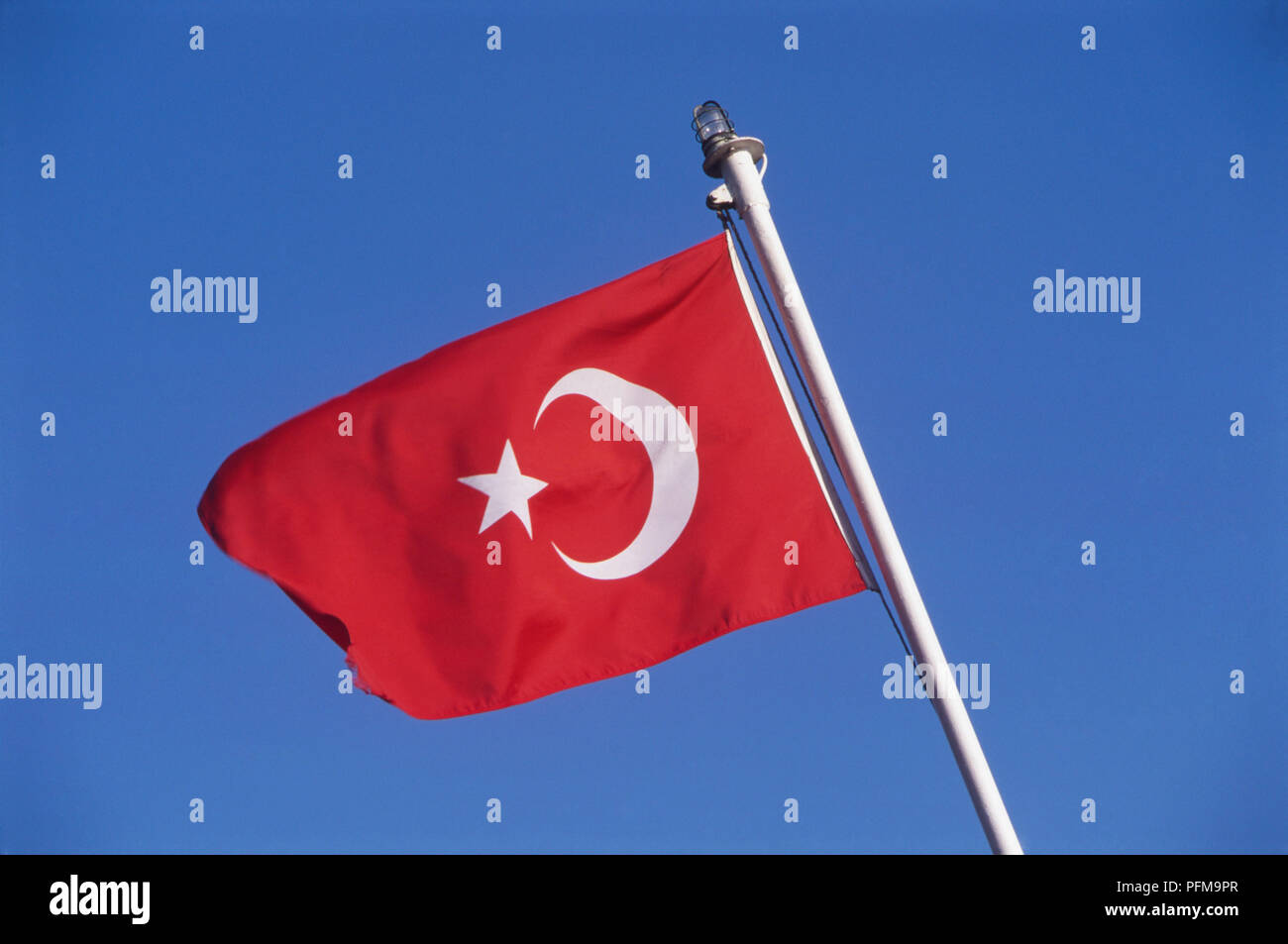 Turkish flag on white flagpole blowing in the breeze, deep blue sky in background. Stock Photo