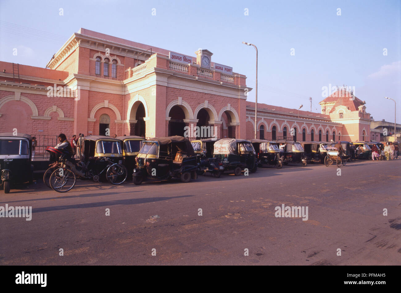 India, Agra, the Fort Railway Station, colonial pink and white building, many towers, clock above entrance, auto-rickshaws parked outside . Stock Photo