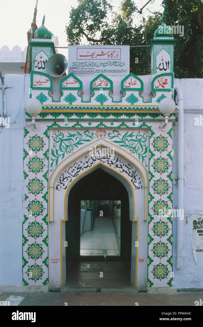 India, Delhi, Dargah Qut Sahit, part of the beautifully decorated exterior of 13th-century shrine, white painted background with intricate green and red designs, flowers and script, adorning archway, still a pilgrim point. Stock Photo