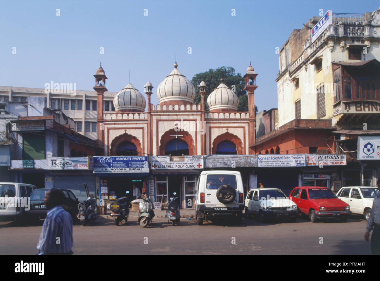 India, Delhi, Fakr-ul-Masjid, red sandstone mosque, white domes and minarets with black stripes, rising above rows of shops and offices along busy street, cars and motorbikes parked in front. Stock Photo