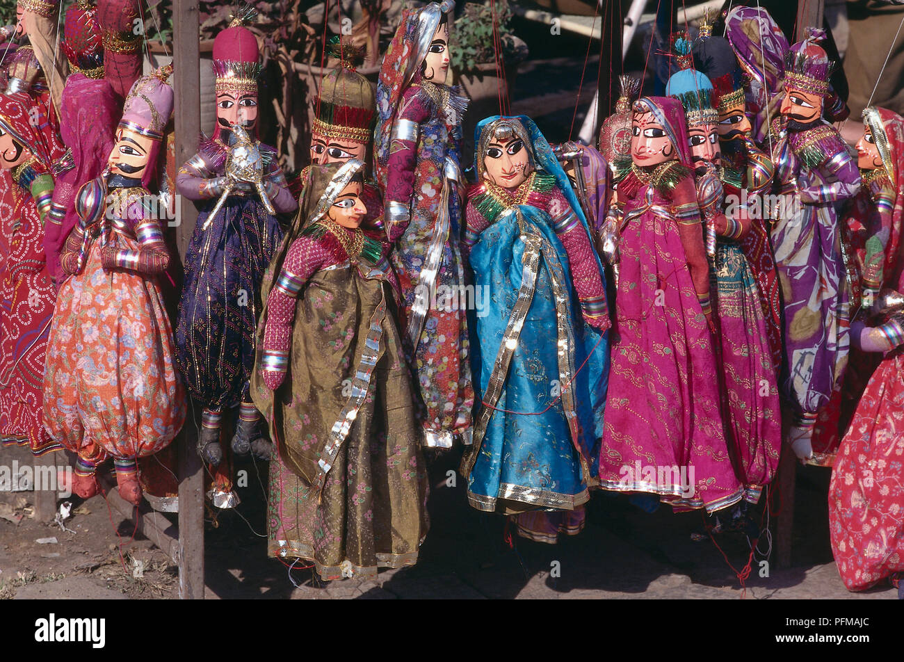 India, Sireh Deori Bazaar, brightly coloured puppets for sale, wearing brightly coloured traditional Indian dress, female puppets wearing vivid saris, male puppets with large black moustache, hanging by red string. Stock Photo