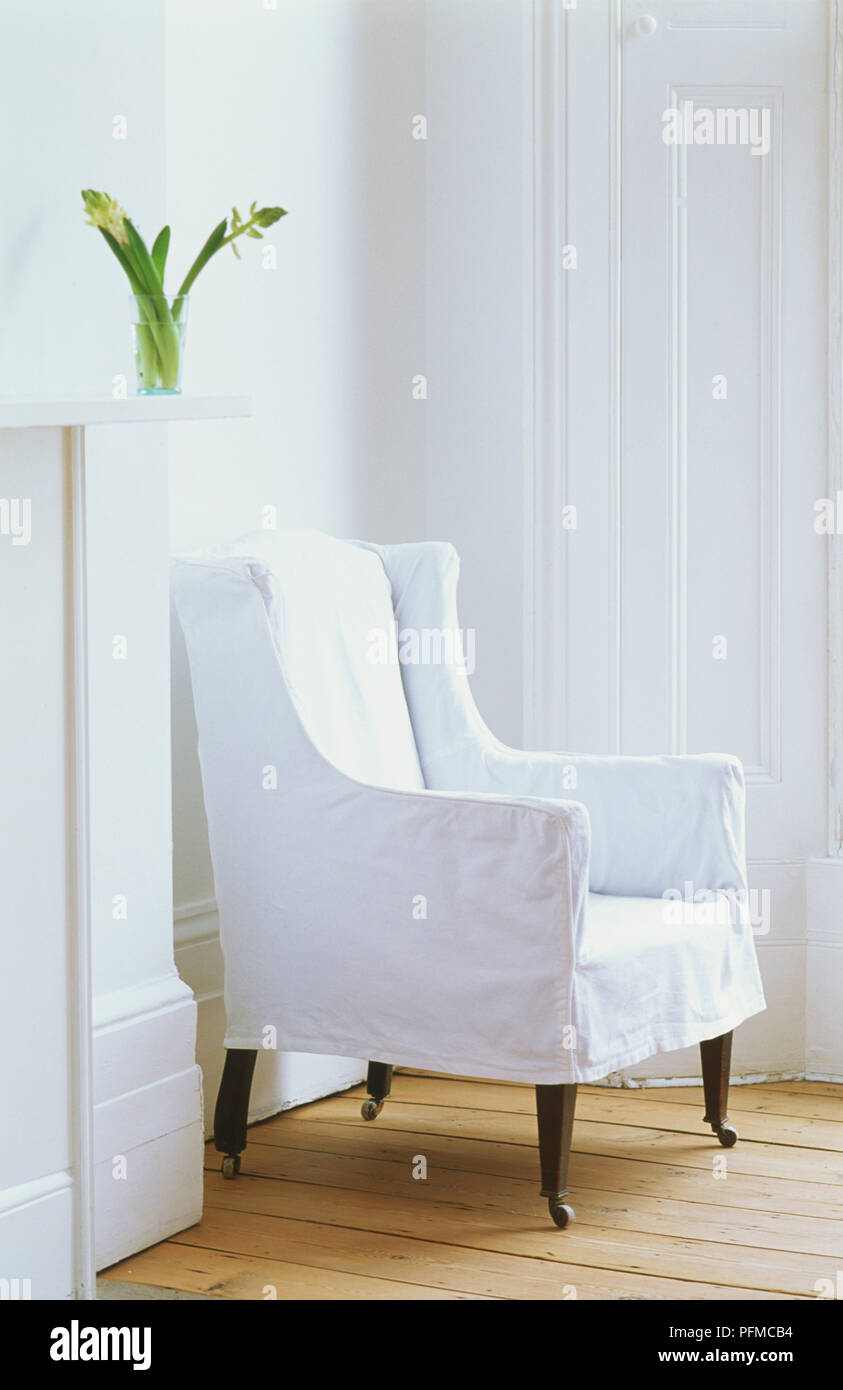 White armchair with wheeled wooden legs in corner of white room with wooden floorboards, side view Stock Photo