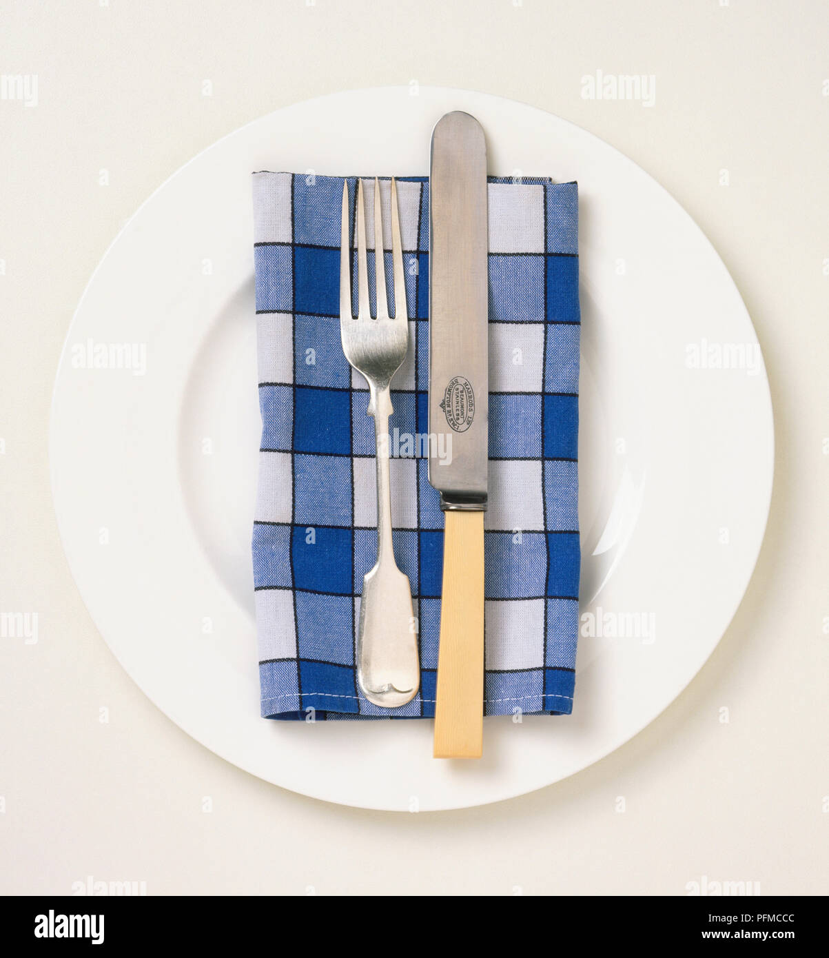 Silver fork and bone-handled knife on a napkin placed on a white plate. Stock Photo