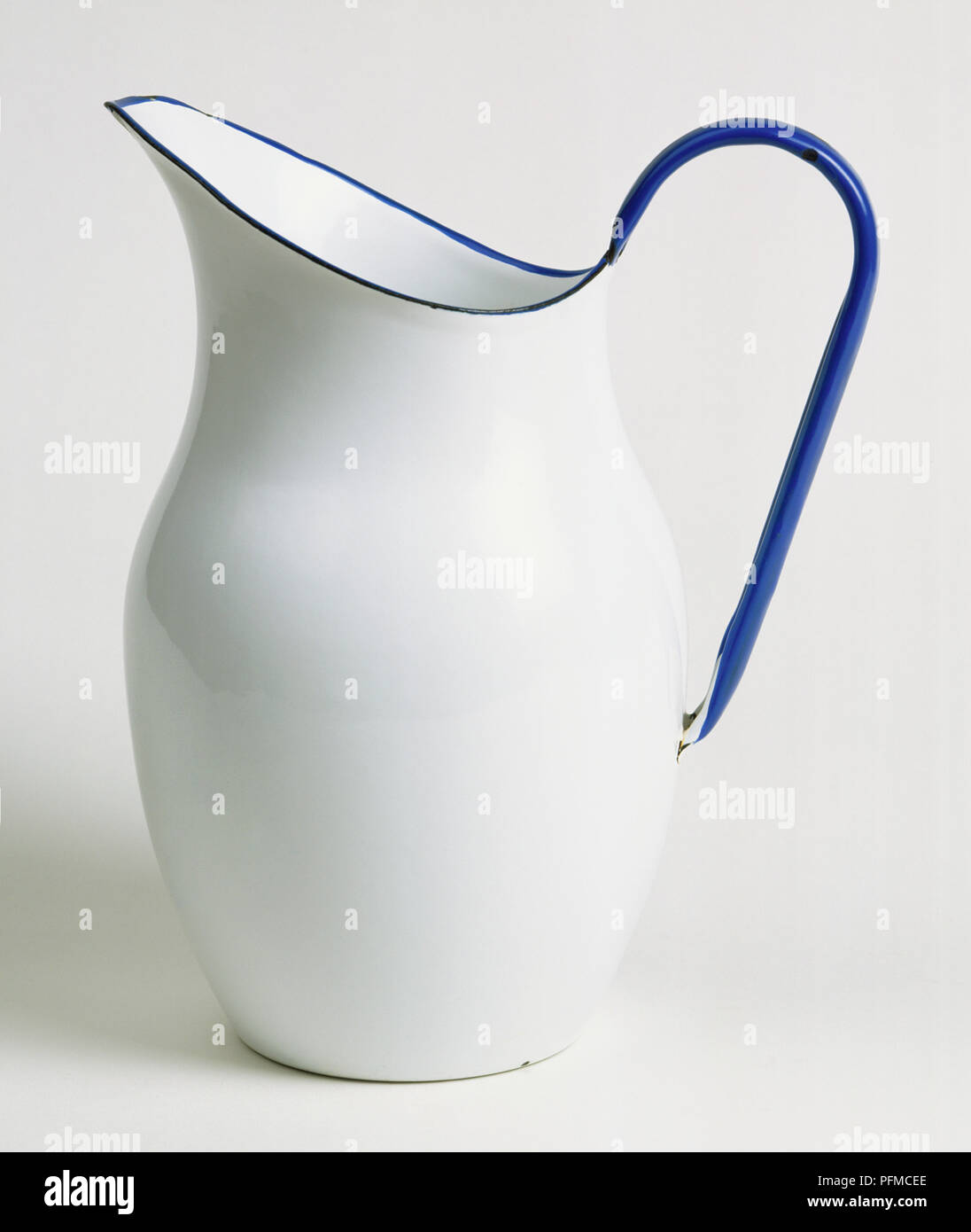 Enamelled metal jug, white with blue rim and handle, side view. Stock Photo