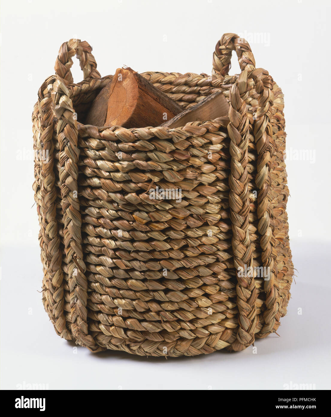 Woven grass log basket, sturdy design with two handles, stored logs visible, angled front view. Stock Photo