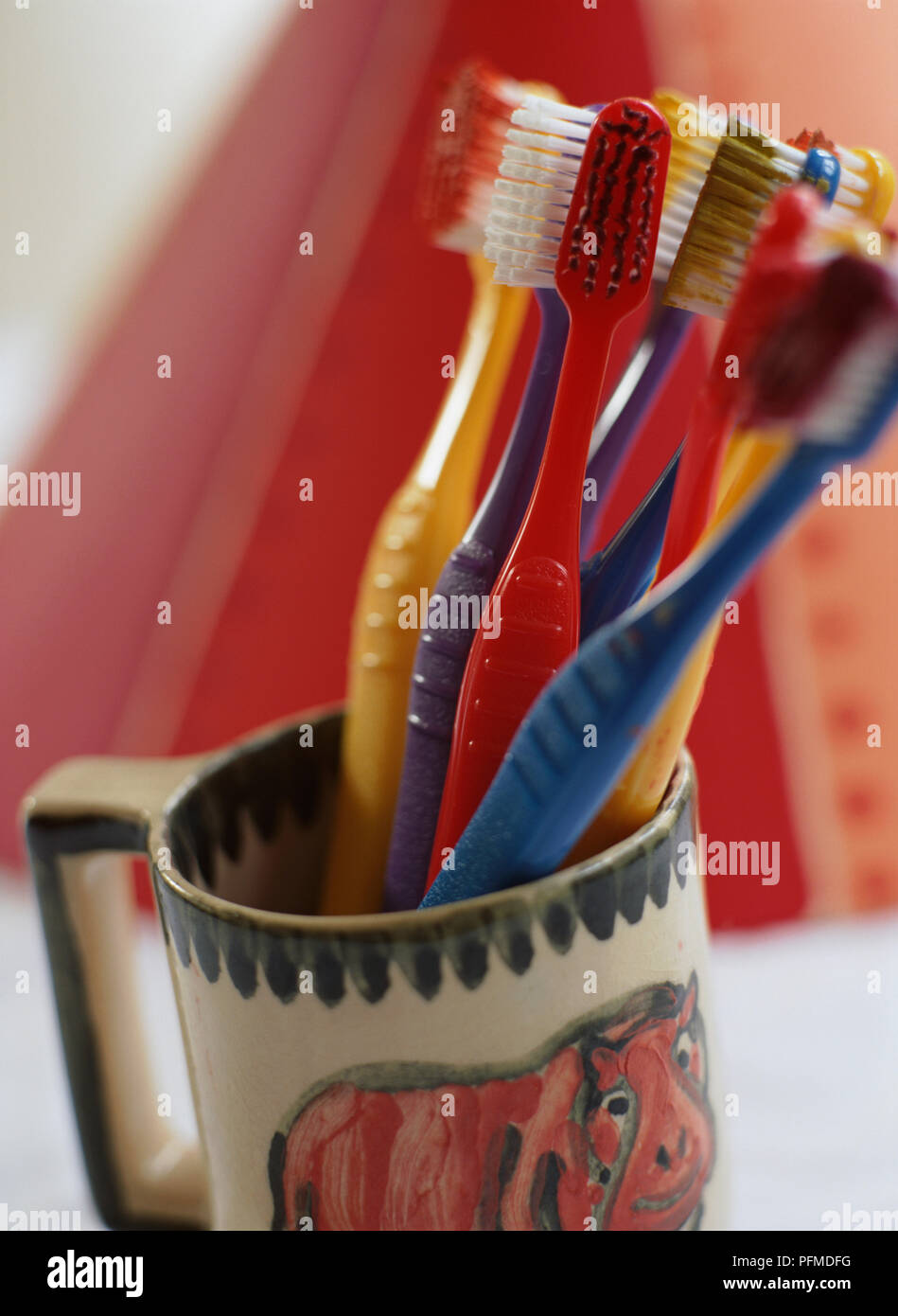 Assorted red, blue and yellow toothbrushes standing in mug, red background. Stock Photo