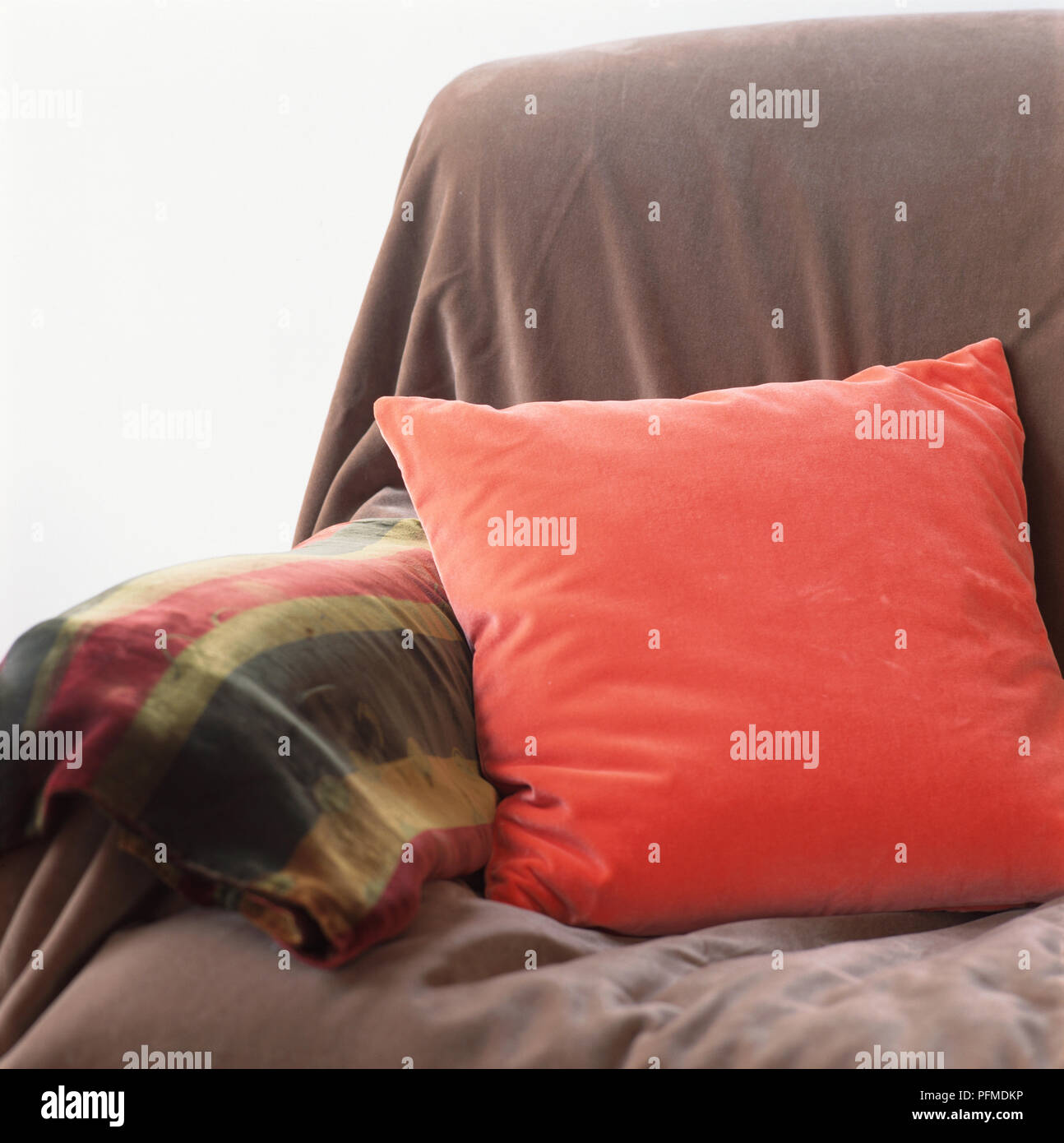 Sofa end covered with purple throw, red cushion scattered by arm, colourful blanket draped over arm. Stock Photo
