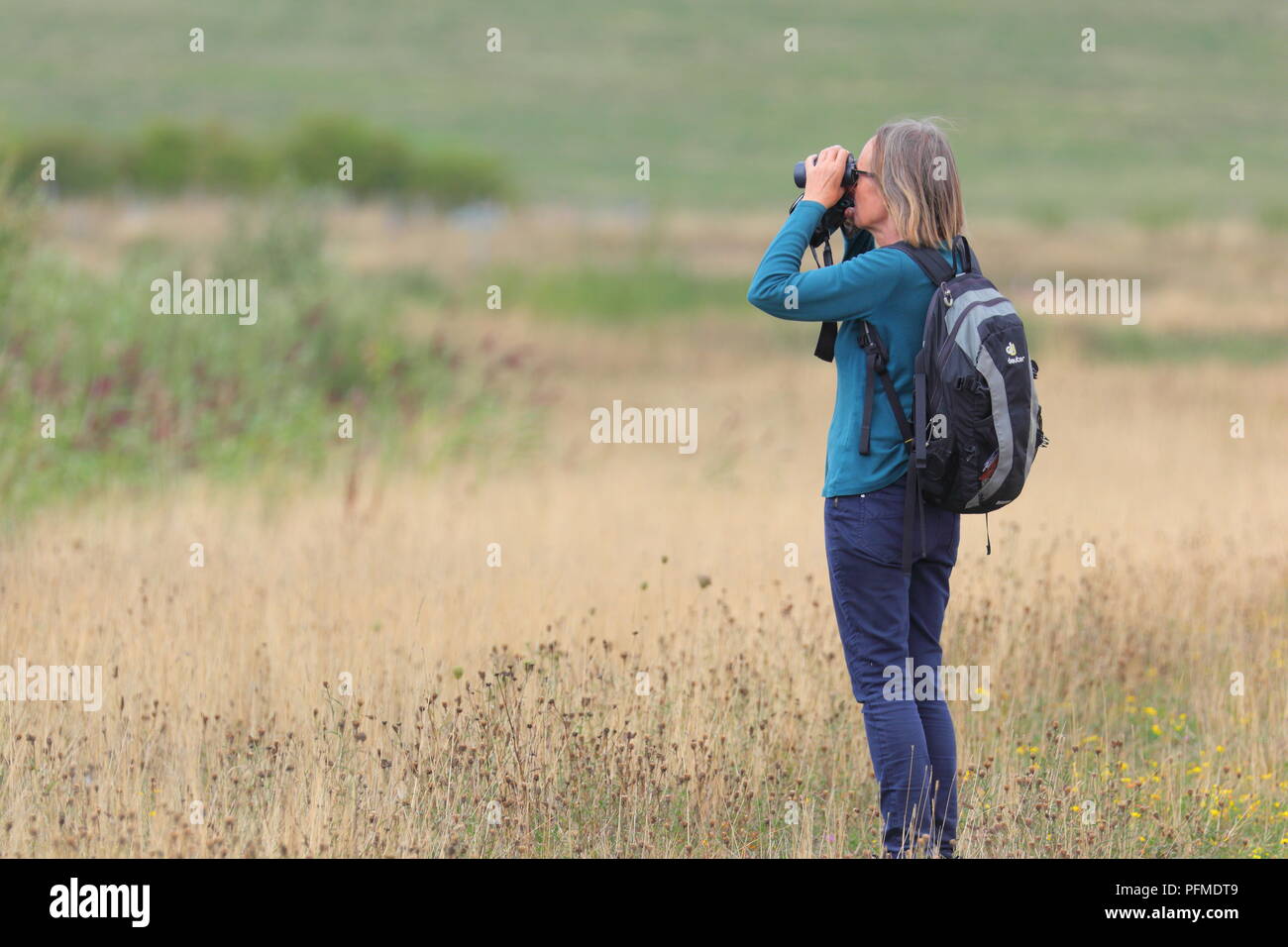 A female birdwatcher looking through binoculars at RSPB St Aidan's ...