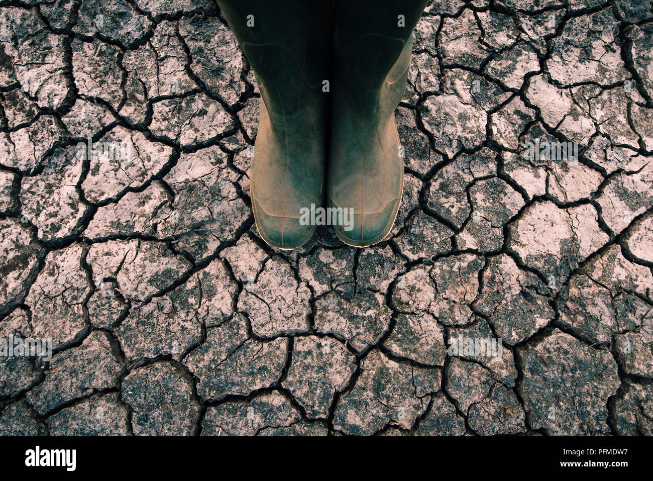 Farmer in rubber boots standing on dry soil ground, global warming and ...