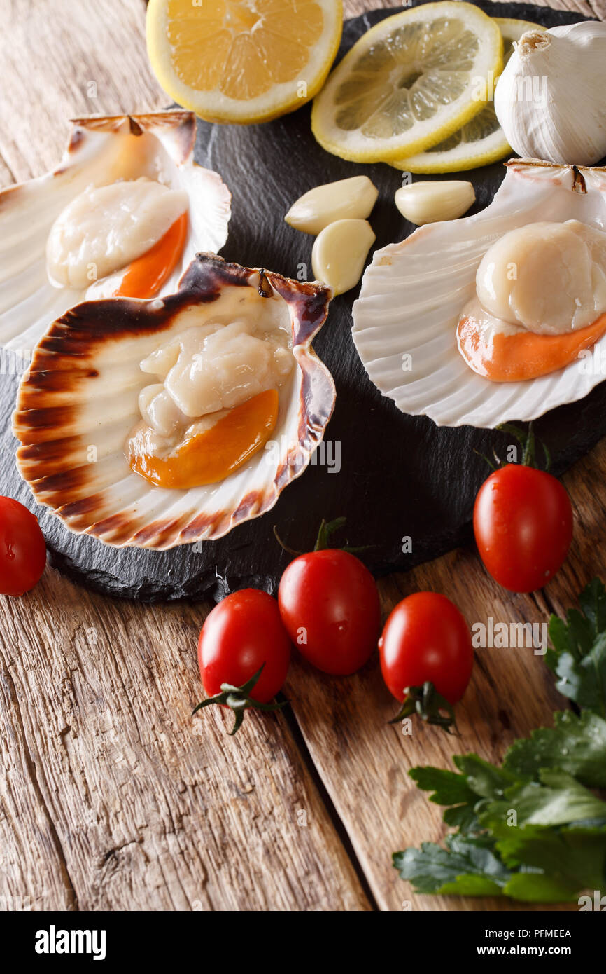 Sea delicacies raw scallops in a seashell and fresh vegetables on a table. vertical Stock Photo