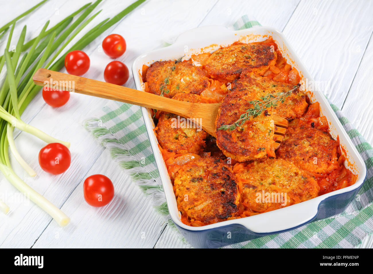 couscous fish patties with onion, carrots and tomato sauce in baking dish with green onion and tomatoes on wooden table, healthy and easy recipe, view Stock Photo