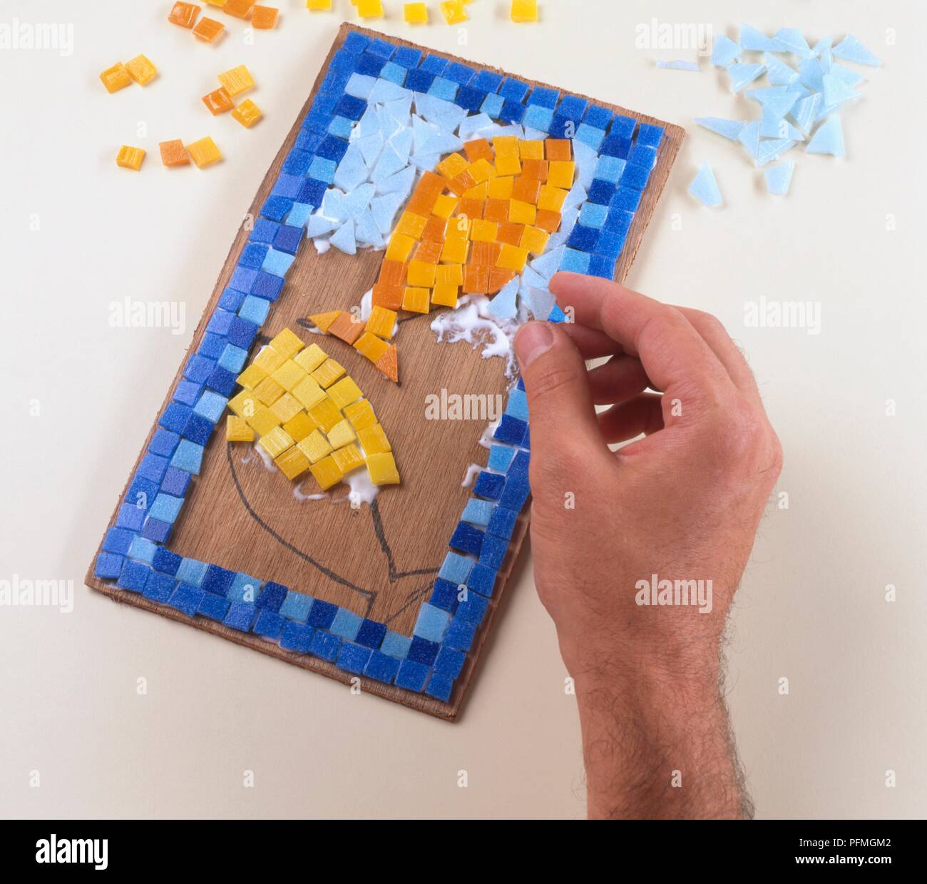Hand gluing small tiles onto mosaic of fish, close-up Stock Photo