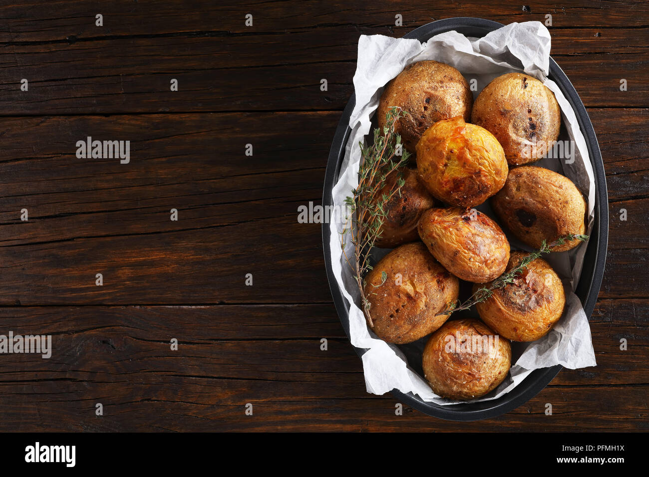 freshly baked whole potatoes with thyme in baking dish on wooden table, horizontal view from above Stock Photo