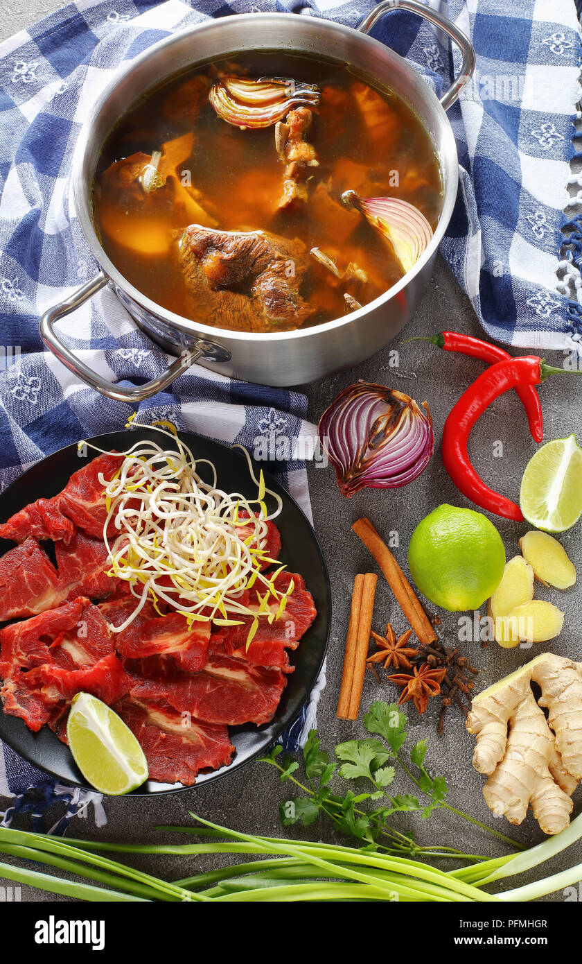 hot beef bone broth and other ingredients for Vietnamese soup Pho Bo, with raw beef, soy sprouts