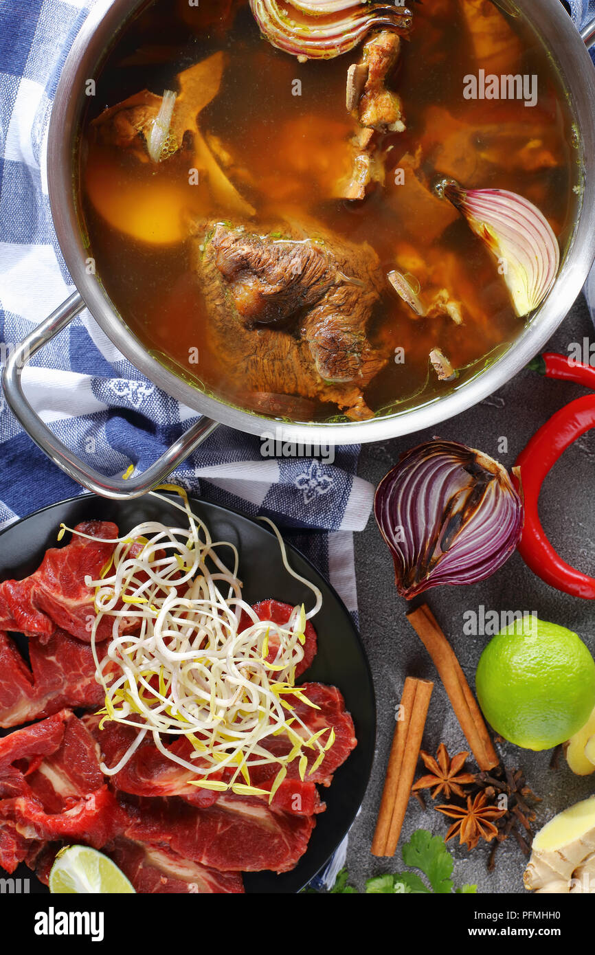 hot beef bone broth and other ingredients for traditional Vietnamese soup Pho Bo with raw beef