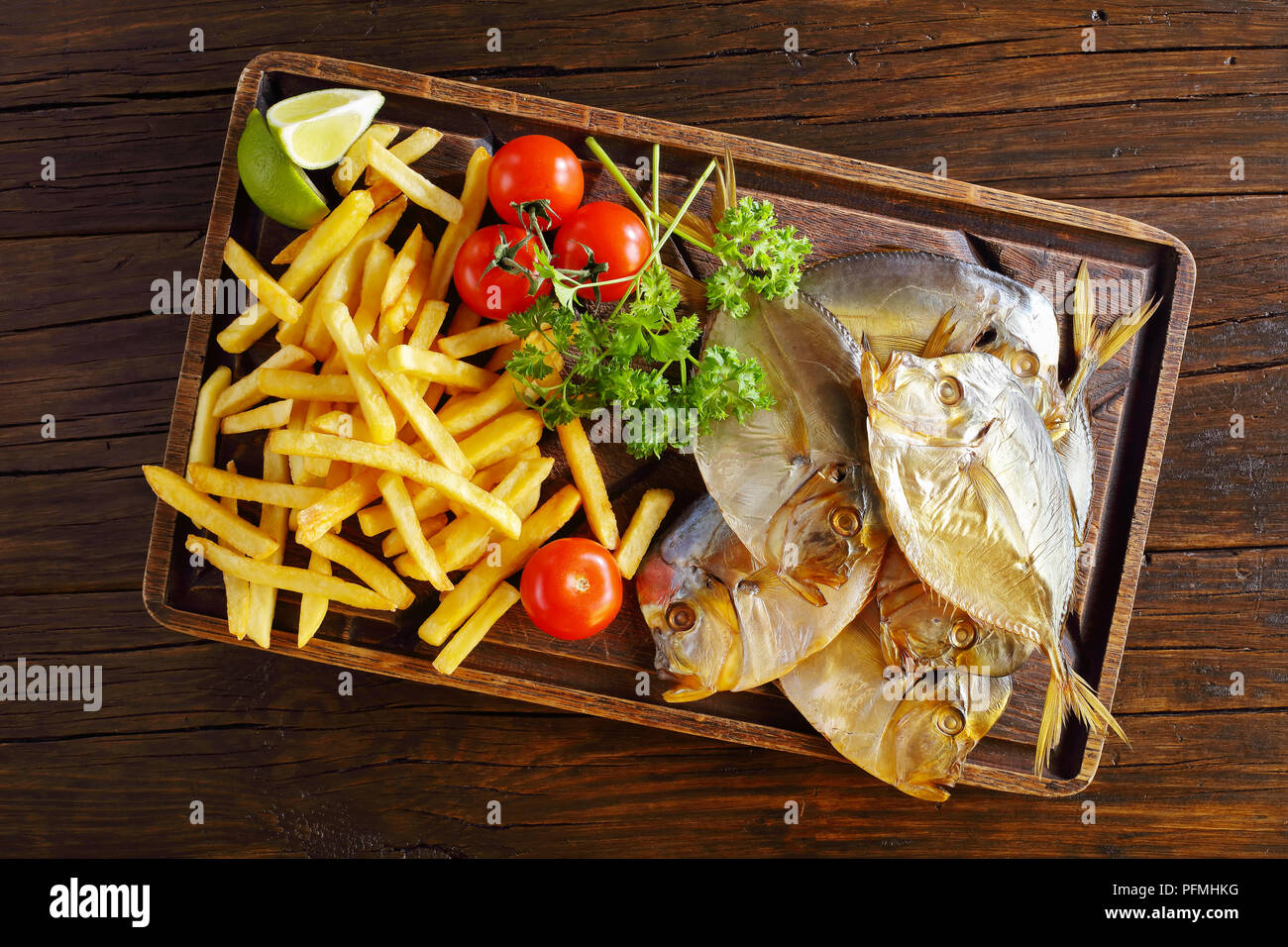 delicious cold smoked moonfish and chips served on brown cutting board on rustic wooden table, view from above Stock Photo